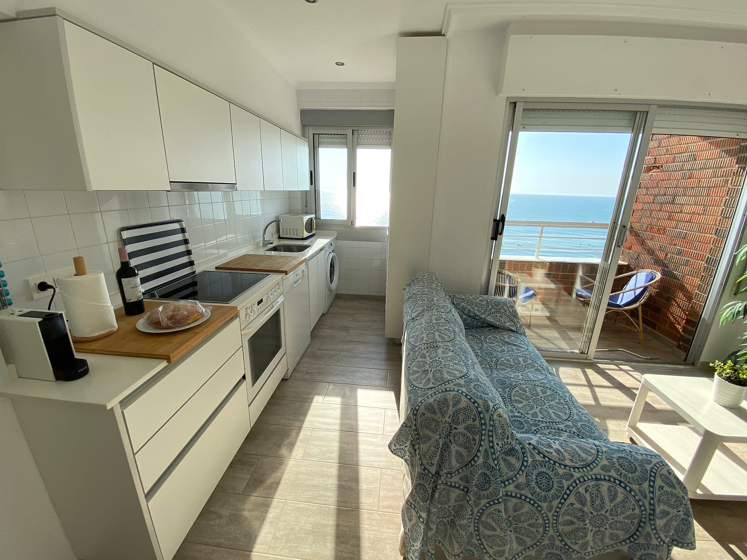 Cocina con vitrocerámica, horno, lavavajillas y lavadora, abierta al salón y con vistas al mar