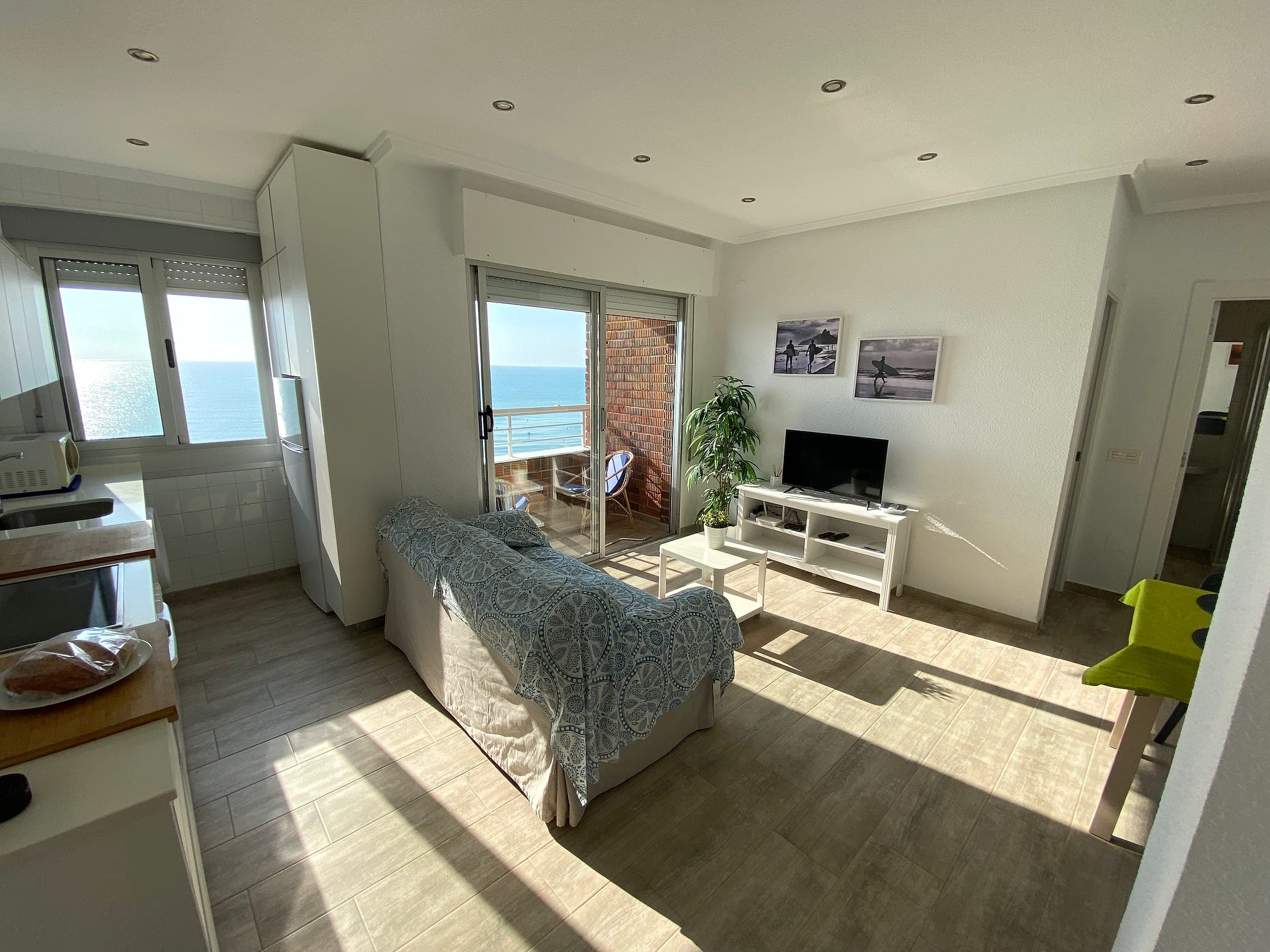 Salón con sofá, televisión y puerta a la terraza, con el mar al fondo